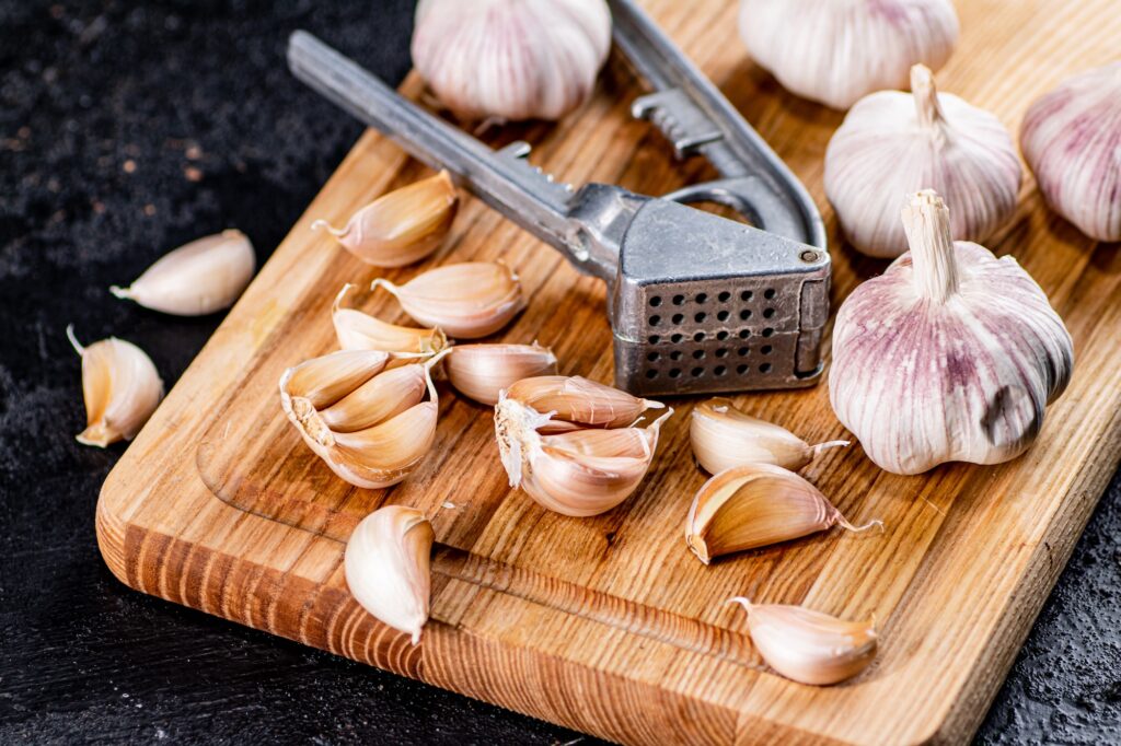 Cloves of garlic on a cutting board with a garlic press. On a black background. High quality photo